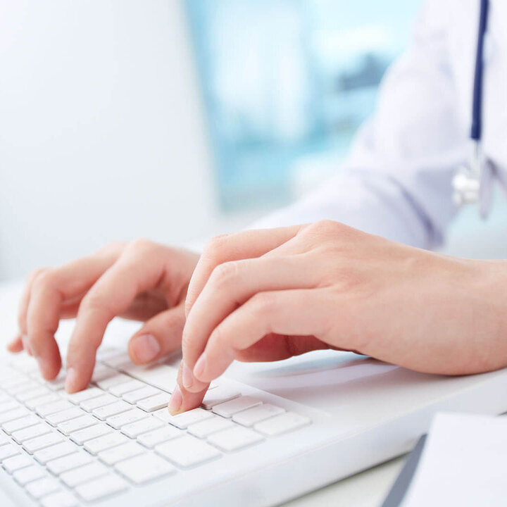 Hände einer Ärztin tippen auf einer weißen Tastatur.