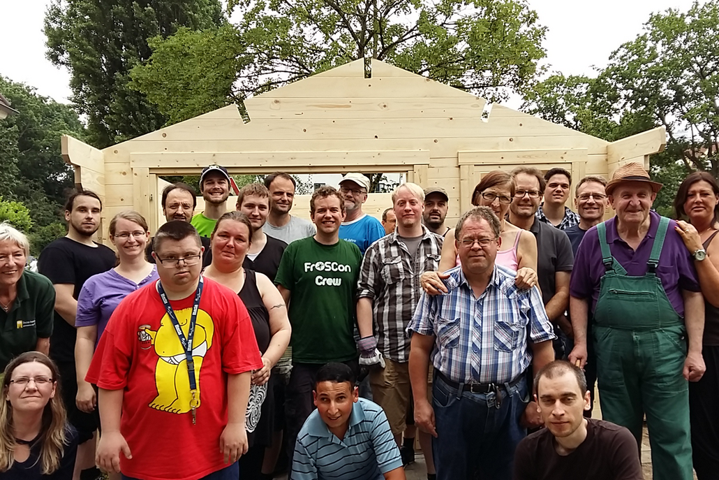 Ein großes Team aus CI-Mitarbeitern und SBK-Riehl-Bewohnern posiert vor der zuvor aufgebauten Holzhütte.
