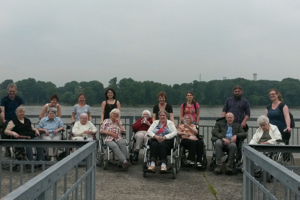Unsere Kollegen, unter anderem Wendy Schrott und Till Krempel, begleiten demenzkrankte Bewohner mit Rollstuhl zum Rhein.
