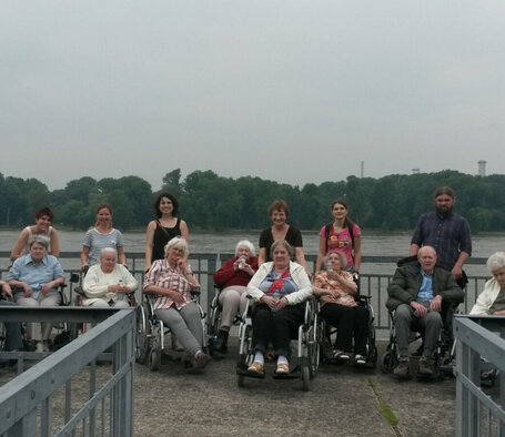 Unsere Kollegen, unter anderem Wendy Schrott und Till Krempel, begleiten demenzkrankte Bewohner mit Rollstuhl zum Rhein.