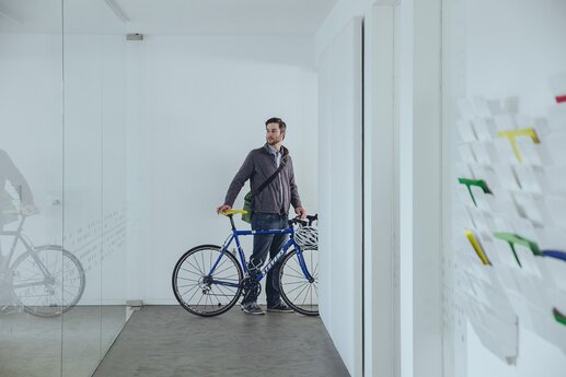 Klemens steht mit seinem blauen Fahrrad im Flur des Kölner Büros.